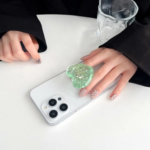 Green glitter heart-shaped expanding phone grip stand attached to white smartphone