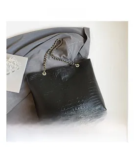 Detail of black crocodile pattern tote bag featuring gold rings and chain strap