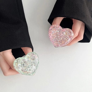 Detail of pink and mint green heart glitter resin phone grips held by hand on white background