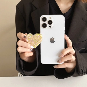 Detail of a heart-shaped phone grip with gold glitter and sequins on a white smartphone