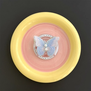 Detail of embroidered butterfly phone stand with pearls on a colorful ceramic plate