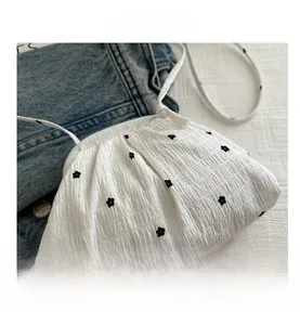 Detailed macro view of white cloud bag featuring black floral embroidery and pleated texture
