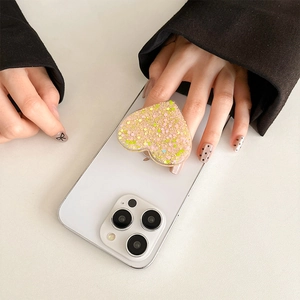 Glittery heart-shaped phone grip with pink and yellow sequins on a white smartphone