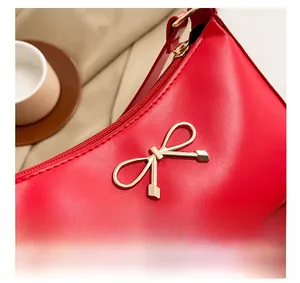 Close-up of a red leather bag featuring a gold bow ornament and zipper closure