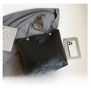Detail of black crocodile texture tote bag with chain strap and silver hardware accents