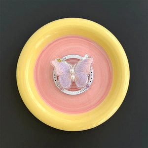 Detail of butterfly phone grip with pink gradient embroidery and white pearls on a tray