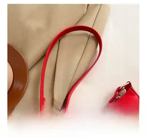 Detail view of red leather shoulder bag showing durable strap attachment and gold bow ornament