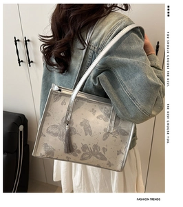 Detail of silver tote bag with grey butterfly print and stylish fringe tassel accessory