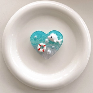 Close-up of heart-shaped resin phone grip with blue ocean waves and pearl dolphin detail