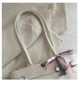 Detailansicht der cremeweißen Beuteltasche mit rosa Seidenband und Karo-Schleife