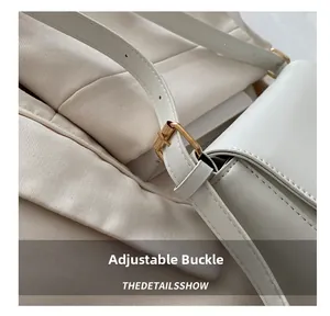 Detailed macro view of the golden adjustable buckle on a white leather shoulder bag strap