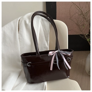 Détail d'un sac cabas en cuir verni marron foncé avec un nœud rose sur une chaise beige