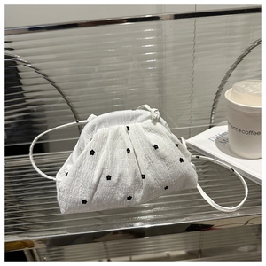 Détail du sac plissé blanc avec broderies de fleurs noires sur un support en verre moderne