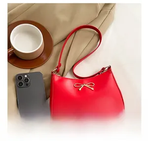 Detail view of red underarm bag with golden bow clasp alongside a phone for size comparison