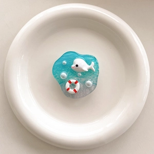 Detail of blue resin ocean phone grip with 3D whale and lifelike pearls on white plate