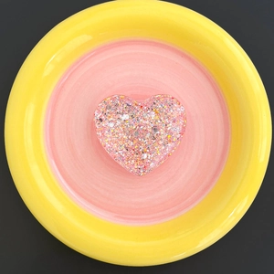 Macro shot of glitter resin heart phone grip with colorful sequins on a dual-tone ceramic dish