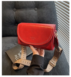 Detail of red leather crossbody bag featuring a woven geometric strap and gold hardware