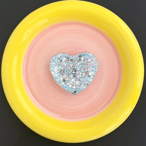 Macro shot of blue and silver glitter heart grip on a yellow and pink ceramic plate