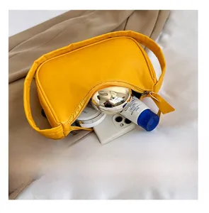 Detail view of mini yellow crescent bag interior capacity showing phone and makeup