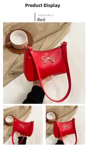 Detail view of a bright red crescent shoulder bag featuring a gold metal bow ornament
