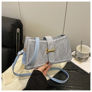 Detail of light blue textured shoulder bag with golden magnetic buckle and pleated side