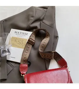 Detail of red vintage leather crossbody bag with wide patterned strap and white stitching