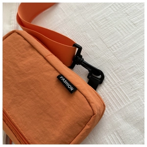 Close-up of orange-brown nylon sling bag featuring a Fashion label and black hardware