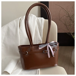 Détail d'un sac cabas en cuir marron foncé brillant avec un nœud rose sur une chaise