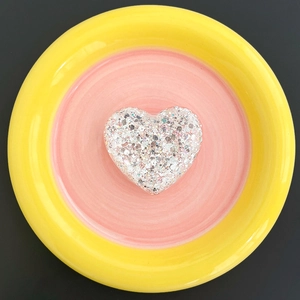 Detail view of heart-shaped glitter phone grip with silver sequins in a ceramic dish