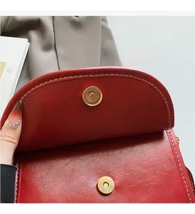Close-up of golden magnetic snap closure on red leather bag with white stitching details