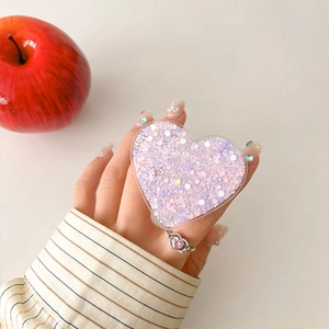 Detail of pink heart-shaped phone grip with glitters and matching ring on hand