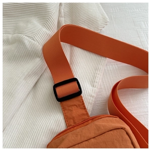Detail of orange nylon mini crossbody bag with woven strap and black plastic buckle