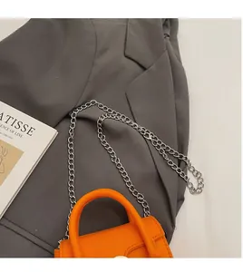Detail of vibrant orange square bag with silver chain strap on a dark grey blazer