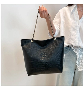 Detail of black crocodile-embossed tote bag with stylish gold chain handles