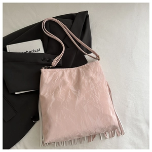 Dettaglio della borsa a secchiello rosa con nappe e trama a pieghe su sfondo bicolore