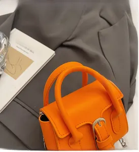 Detail of orange faux leather handbag showing pebbled texture and silver metal buckle