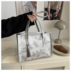 Detail of white butterfly print tote bag with silver metallic handle and tassel charm