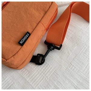 Macro detail of orange nylon crossbody bag showing the fashion label and durable strap
