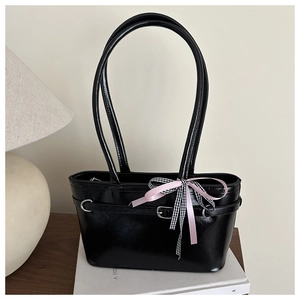 Détail du sac à main noir brillant avec un nœud en satin rose et à carreaux et bandoulière