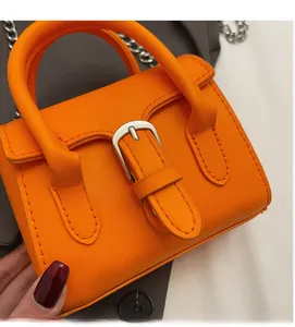 Close-up of bright orange mini handbag with decorative silver buckle and chain strap