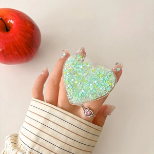 Macro detail of heart-shaped phone grip with green sequins and acrylic finish