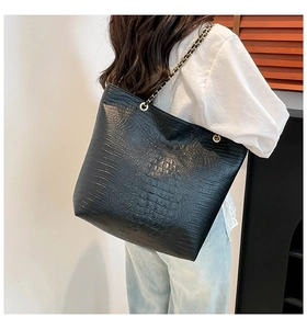 Detail of black crocodile-embossed tote bag with gold chain and leather shoulder strap