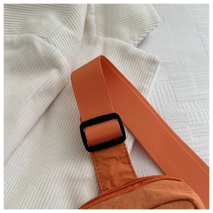 Detail of orange nylon chest bag featuring adjustable black buckle and woven strap