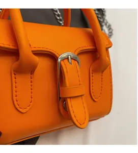 Close-up of bright orange square handbag showing fine leather texture and silver buckle