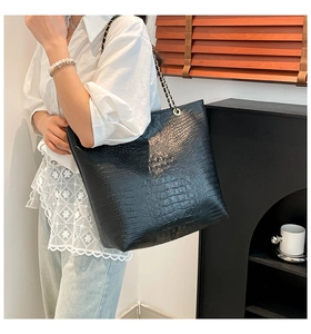 Detail of black crocodile texture tote bag with metal chain strap worn on shoulder
