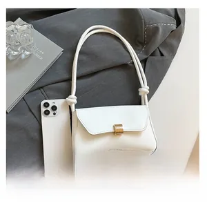 Close-up of white leather shoulder bag with gold square buckle and phone for scale