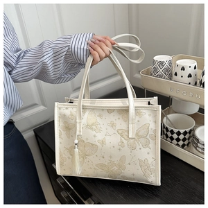 Detailed view of the butterfly print and white tassel pendant on an elegant tote bag