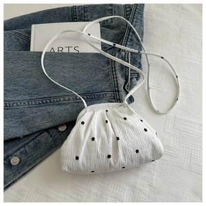 Détail du sac plissé blanc à motif floral posé sur un vêtement en denim bleu foncé