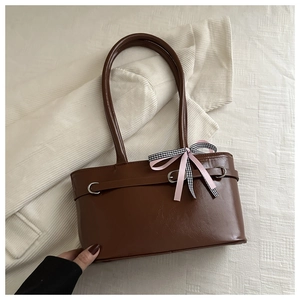 Détail du sac à main en cuir marron foncé avec boucle argentée et nœud en ruban rose