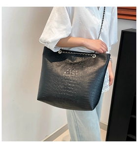 Detail of black crocodile texture tote bag with metallic chain straps and metal eyelets
